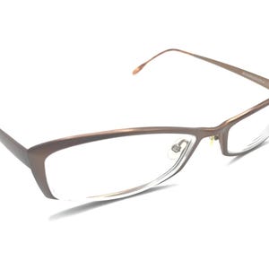 May include: Brown metal frame eyeglasses with clear lenses. The frame has a cat-eye shape.