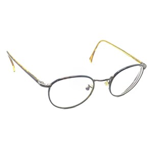 Puede incluir: Gafas con monturas redondas de carey oscuro, un puente fino y patillas delgadas de color claro. Las lentes transparentes están colocadas dentro de los aros circulares, y el diseño incluye almohadillas nasales ajustables.