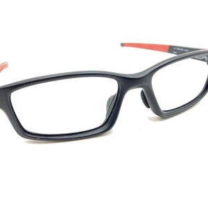May include: Black framed eyeglasses with red accents on the arms. The glasses have a rectangular shape and clear lenses.