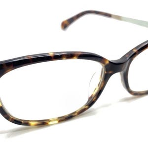 May include: Tortoiseshell-patterned eyeglasses with a cat-eye shape. The frames are a mix of brown and yellow, with silver-colored arms. The lenses are clear, and the glasses are set against a white background.