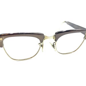 Könnte beinhalten: Braune Kunststoff-Brille mit goldenen Metall-Akzenten und klaren Gläsern.