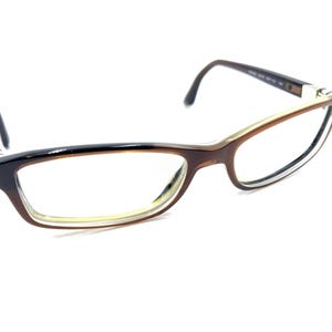 Può includere: Occhiali da vista marroni e neri con lenti trasparenti. La montatura ha un sottile accento argentato.