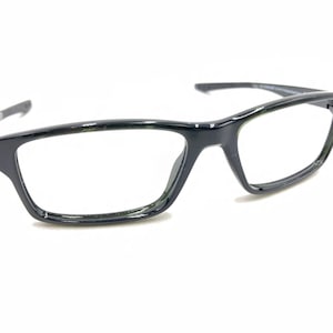 May include: Black plastic framed eyeglasses with clear lenses. The frames have a rectangular shape with a slight curve at the top.