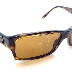 May include: Tortoiseshell sunglasses with brown tinted lenses. The rectangular frames have a dark brown and amber pattern. A gold-colored emblem is on the temples. The sunglasses are a classic accessory.