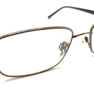 May include: Eyeglasses with a brown metal frame and clear lenses. The rectangular frames have a modern design. The temples are dark brown. The glasses are set against a white background.