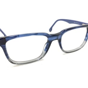 May include: Blue and clear eyeglasses with a rectangular frame. The frames have a marbled effect, with shades of blue and clear. The temples are a solid blue color. The glasses are set against a white background.