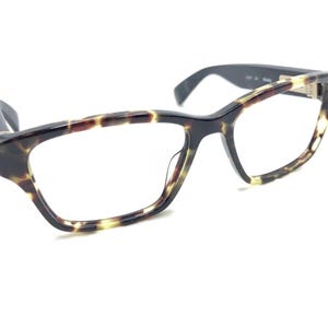 Puede incluir: Gafas de pasta de carey con montura negra y lentes transparentes.