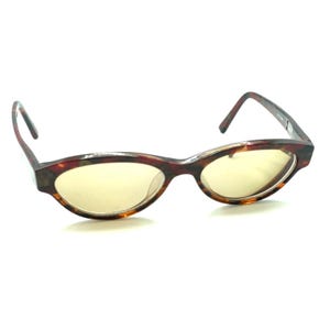 May include: Oval-shaped eyeglasses featuring a brown and black tortoiseshell pattern frame. The lenses are tinted a light, translucent yellow color. The frame has a smooth, polished finish with thin, curved temples extending from the sides.