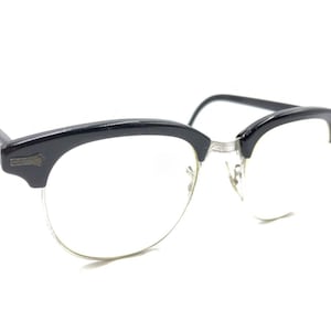 May include: Black plastic framed glasses with clear lenses. The glasses have a browline style with a thin metal bridge.