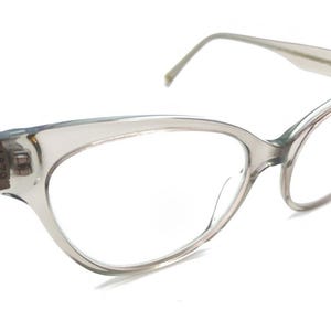 May include: A pair of clear-framed eyeglasses with a cat-eye shape. The glasses have a light gray tint and are set against a white background. The temples have the number "1879" printed on them.