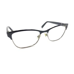 Puede incluir: Un par de gafas con una montura superior de color azul marino oscuro y un borde inferior de metal fino en tono plateado. Las gafas tienen lentes transparentes, almohadillas nasales ajustables y patillas delgadas en los extremos.