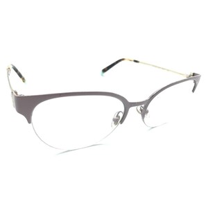 May include: Semi-rimless eyeglasses featuring a matte taupe-colored metal frame with a cat-eye silhouette. The thin temples are gold-toned with tortoiseshell-patterned acetate tips. The nose pads are clear and adjustable, attached to the bridge.