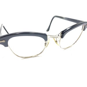 Puede incluir: Gafas de pasta negras de estilo ojo de gato con detalles en metal plateado. Las gafas tienen un estilo vintage.