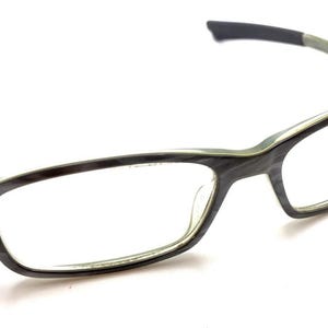 May include: Rectangular eyeglasses featuring a dark gray and black wood-grain pattern on the frames. The temples are a translucent light green with dark gray tips. The bridge and rims are integrated into a single continuous frame structure.