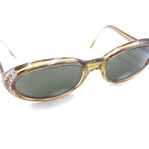May include: A pair of brown oval-shaped sunglasses with rhinestones on the frame. The sunglasses have dark lenses.