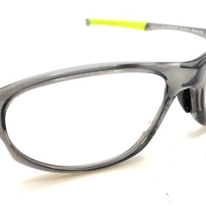 May include: Gray eyeglasses with clear lenses and a neon yellow accent on the temple. The frames have a sporty, wraparound design. The glasses are set against a white background.