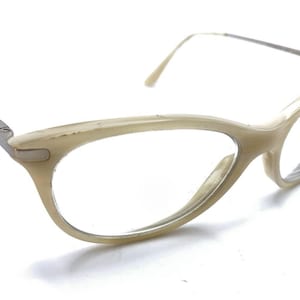 May include: Cat-eye glasses featuring a glossy, cream-colored frame with a subtle marbled texture. The temples are constructed from thin, silver-toned metal, providing a contrast to the thicker, rounded front rims of the eyewear.