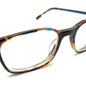 May include: Eyeglasses with a rectangular frame featuring a tortoiseshell pattern in shades of brown, black, and tan, accented with bright blue details along the top rim and temples. The thin metal arms have brown and tan tips at the ends.