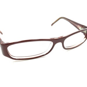 Pode incluir: Um par de óculos de cor bordô com armação retangular e lentes transparentes.