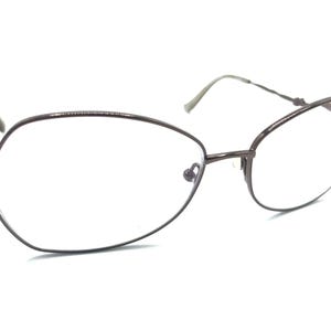 Puede incluir: Un par de gafas de metal marrón con forma de ojo de gato. Las gafas tienen un fino marco de metal y lentes transparentes.