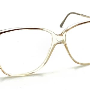 May include: Clear-framed eyeglasses with a light brown tint. The glasses have a rectangular shape with rounded edges and thin, metal arms. The lenses are clear, and the frame is made of a transparent material.