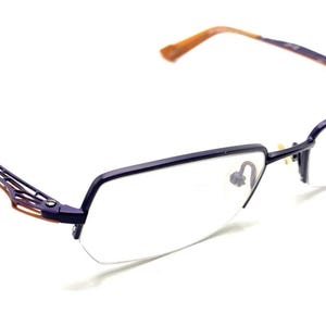 May include: Eyeglasses with a dark blue frame and clear lenses. The temples have a decorative, openwork design with brown accents. The earpieces are brown. The glasses are set against a white background.