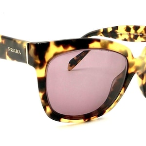 May include: Tortoise shell sunglasses with a brown and gold frame and dark purple lenses. The sunglasses have the word "PRADA" written on the side of the frame.