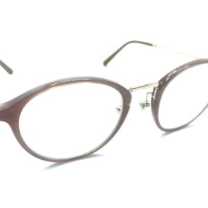 May include: Oval-shaped eyeglasses with a brown frame and silver-colored temples. The lenses are clear, and the glasses have a modern, minimalist design. The frame appears to be made of a durable plastic material.