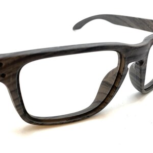May include: Dark gray eyeglasses with a rectangular frame. The glasses have a wood grain pattern and clear lenses. The temples curve slightly for a comfortable fit. The glasses are set against a white background.