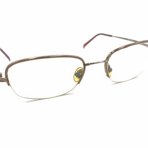 Puede incluir: Un par de gafas de metal dorado con lentes transparentes. Las gafas tienen un diseño sin montura y una forma ligeramente ovalada.