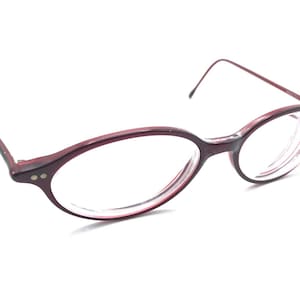 Puede incluir: Un par de gafas ovaladas de color burdeos con lentes transparentes.