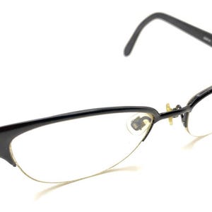 Puede incluir: Gafas negras con diseño de media montura. Las monturas son negras con un acento plateado en las patillas. Las lentes son transparentes y las gafas tienen un estilo clásico y elegante.