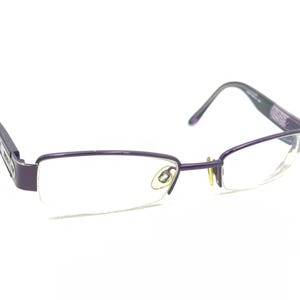 Puede incluir: Gafas de metal con montura morada y lentes transparentes. Las gafas tienen un diseño simple y moderno.