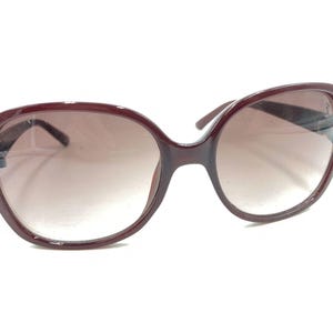 Puede incluir: Gafas de sol de plástico color burdeos con montura redonda de gran tamaño y lentes marrones degradados.