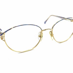 Puede incluir: Gafas de metal dorado con detalles azules en las patillas. Las gafas tienen una forma redondeada y ovalada.