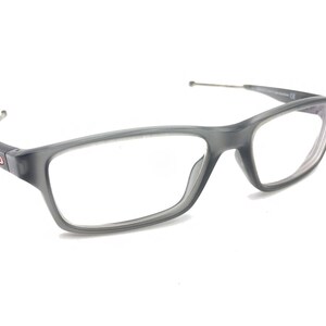 May include: Gray eyeglasses with a clear lens and a thin metal arm. The frame is made of a semi-transparent plastic.