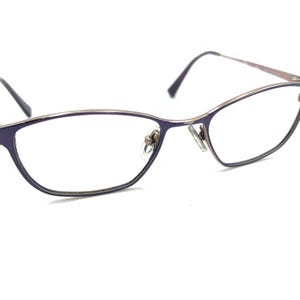 May include: A pair of silver-toned spectacles with purple frames and clear lenses.