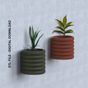 Könnte beinhalten: Zwei Wand-Blumenkästen mit grünen und braunen gerippten Designs. Jeder Blumenkasten enthält eine Topfpflanze mit grünen Blättern.