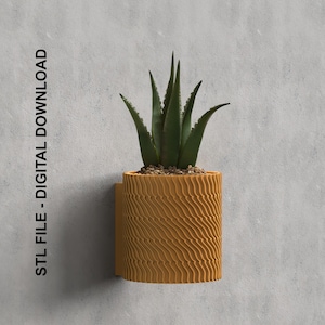 Op de afbeelding: Een 3D-geprinte wandpot met een golvende textuur in mosterdgele kleur. De pot bevat een kleine succulent.