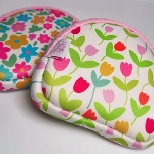 Peut inclure: Deux petits porte-monnaie ronds avec un motif floral. Les bourses ont un fond blanc avec des fleurs colorées roses, jaunes, bleues et oranges. Les bords sont bordés d'un passepoil rose, et chacun a une fermeture éclair rose et une petite étiquette.