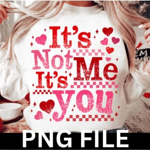 Puede incluir: Sudadera blanca con el texto "It's Not Me It's You" en letras rojas y rosas. El diseño incluye formas de corazón y diamantes. La parte inferior de la imagen tiene el texto "PNG FILE" en negro.