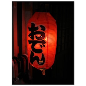 May include: A red paper lantern with black Japanese characters that read "Machan" hanging in a dark room.