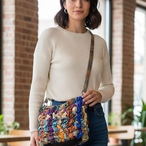 Könnte beinhalten: Handgefertigte Umhängetasche mit einem strukturierten, gerüschten Design. Sie hat eine Mischung aus blauen, violetten, orangefarbenen und braunen Stoffen. Die Tasche hat einen braunen Lederriemen und einen dunkelbraunen Boden.