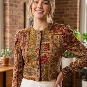 Könnte beinhalten: Eine langärmelige, kurz geschnittene Jacke mit einem mehrfarbigen Patchwork-Muster in Rot-, Gold- und Brauntönen. Das Kleidungsstück hat einen Rundhalsausschnitt, eine Knopfleiste vorne mit fünf strukturierten Metallknöpfen und Schulterpolster.