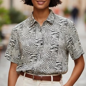 May include: A short-sleeved button-down shirt featuring a black and white patchwork pattern of animal prints including zebra stripes and leopard spots, paired with high-waisted cream-colored trousers and a brown leather belt with a silver buckle.