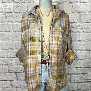 May include: A brown and white plaid flannel shirt with a faded look. The shirt has a button-up front and long sleeves. The shirt is being worn over a white tank top and a long beaded necklace.