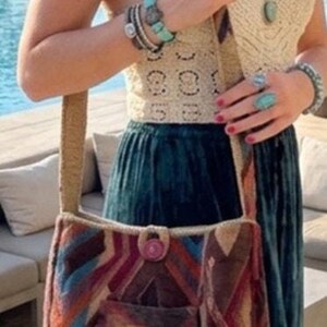 Puede incluir: Un bolso de hombro con un patrón geométrico multicolor en tonos rojo, azul, naranja y marrón. El bolso tiene una sola correa ancha, un bolsillo frontal central y un cierre de botón circular en la parte superior de la abertura principal.