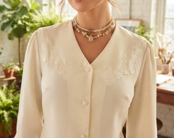 Op de afbeelding: Een crèmekleurige blouse met lange mouwen, voorzien van een brede, puntige kraag met subtiel ton-sur-ton bloemenborduurwerk, een V-hals, een knoopsluiting aan de voorzijde met bijpassende knopen en mouwen met manchetten.