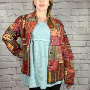 Könnte beinhalten: Eine rote, braune und gelbe Patchworkjacke mit Knopfleiste. Die Jacke hat eine gesteppte Textur und ist aus verschiedenen Stoffen gefertigt.
