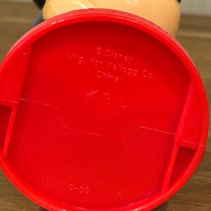 May include: A red plastic Mickey Mouse figurine base with the text "&copy; Disney Mfg. for Kellogg Co. China". The figurine has a black ear and a tan head.